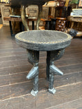 A dark carved wooden stool with a round seat and four sculpted legs