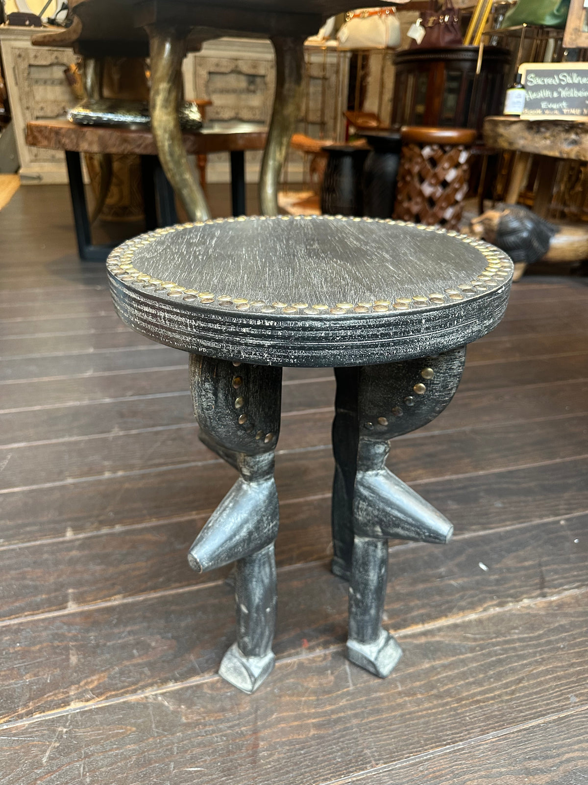 A dark carved wooden stool with a round seat and four sculpted legs