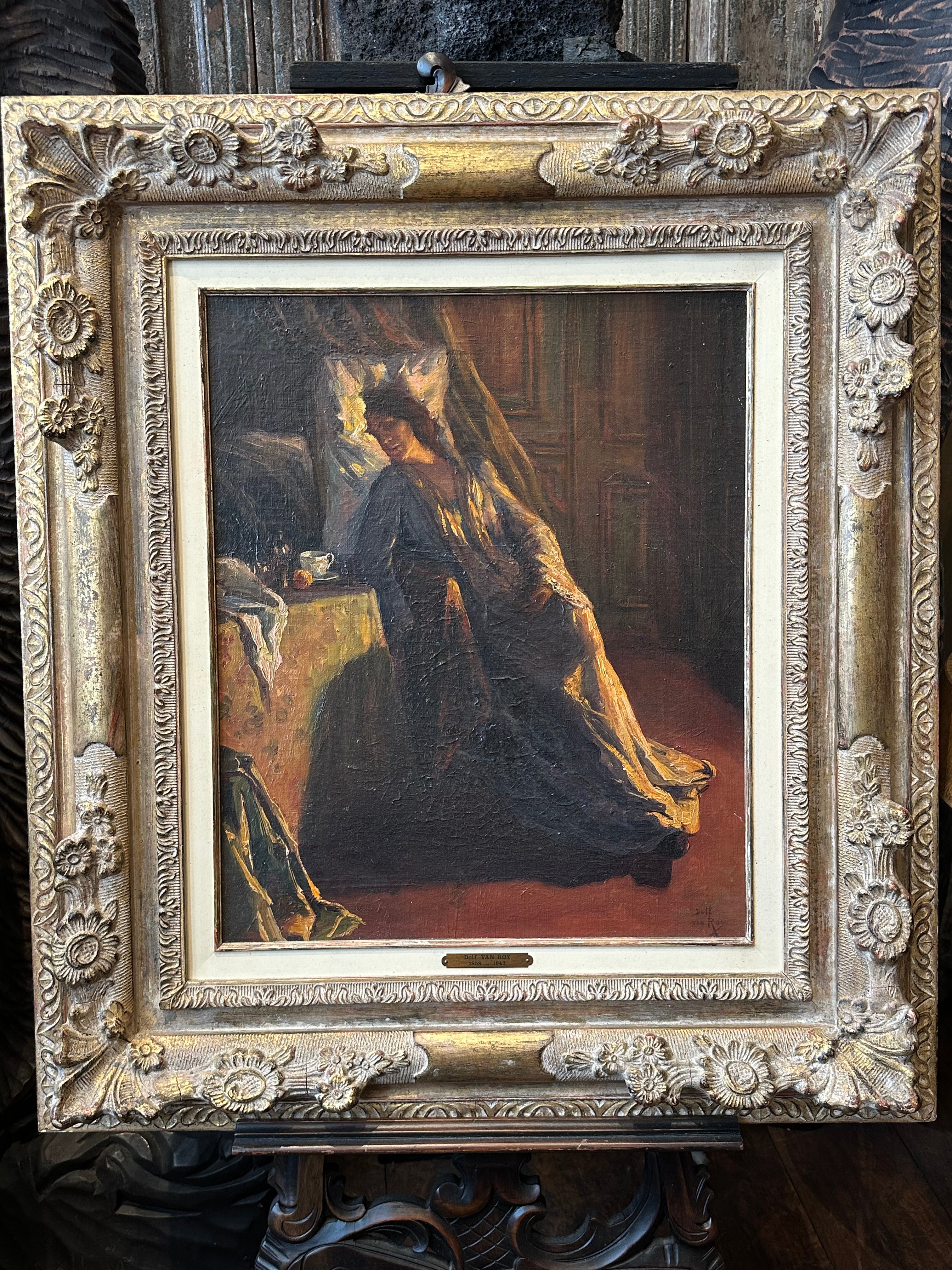 An oil painting of a woman in a dark dress seated indoors, housed in an ornate carved gold frame.