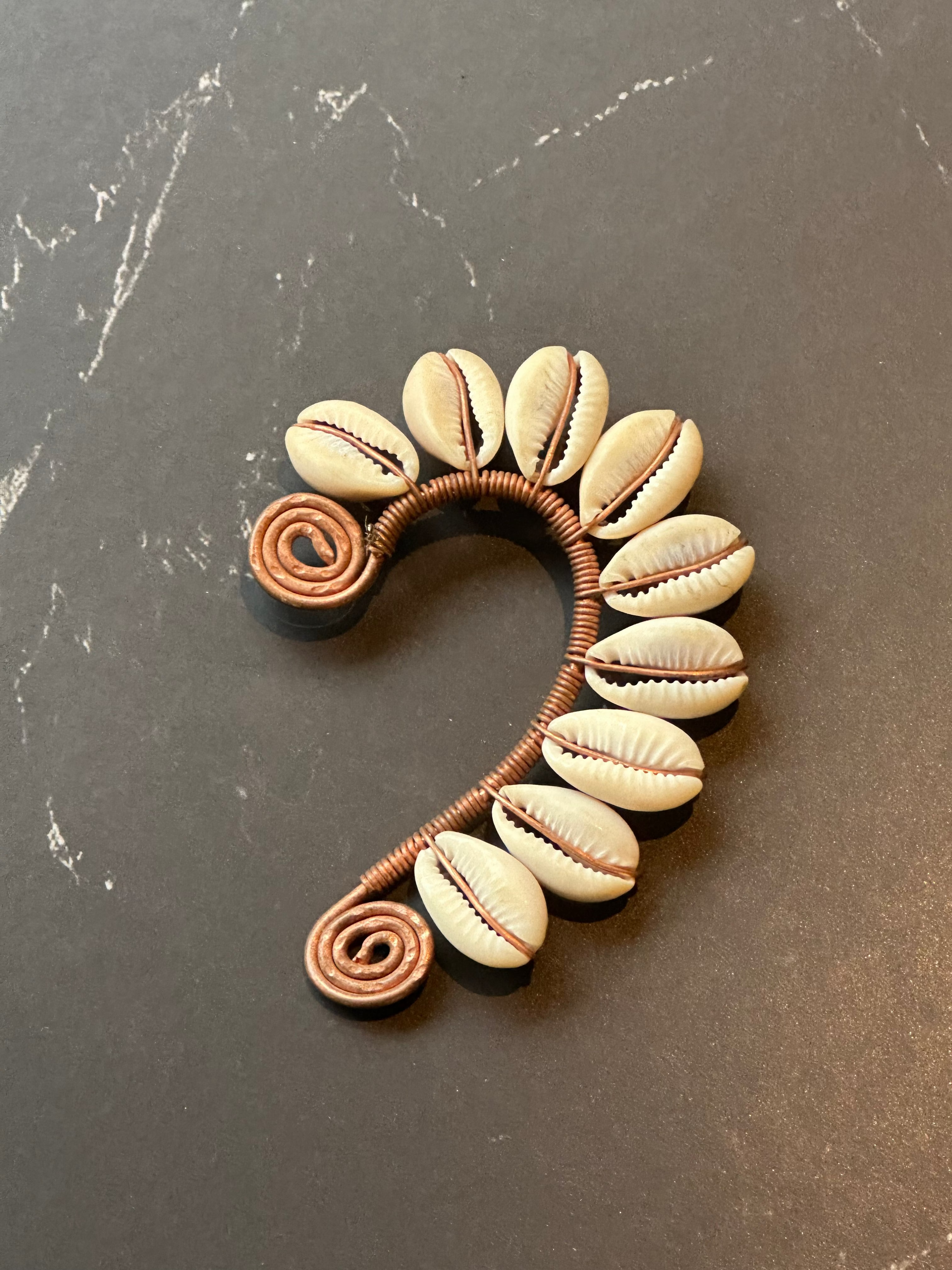 handmade ear-cuff featuring natural cowrie shells and copper-colored wrapped wire spirals at the ends
