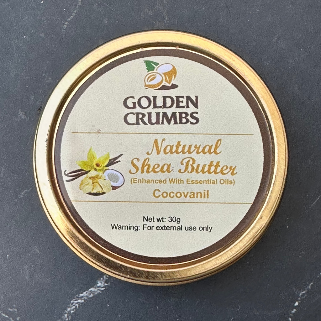 A round tin of Golden Crumbs Natural Shea Butter (Cocovanil) with a gold-colored rim and a beige label, placed on a dark gray stone surface.