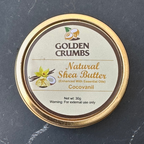 A round tin of Golden Crumbs Natural Shea Butter (Cocovanil) with a gold-colored rim and a beige label, placed on a dark gray stone surface.
