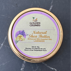 A round tin of Golden Crumbs Natural Shea Butter in Lavender, featuring a gold-colored metal rim and a lavender-themed label, set on a dark gray marble surface.