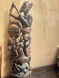 A tall carved wooden sculpture depicting stacked human figures playing musical instruments