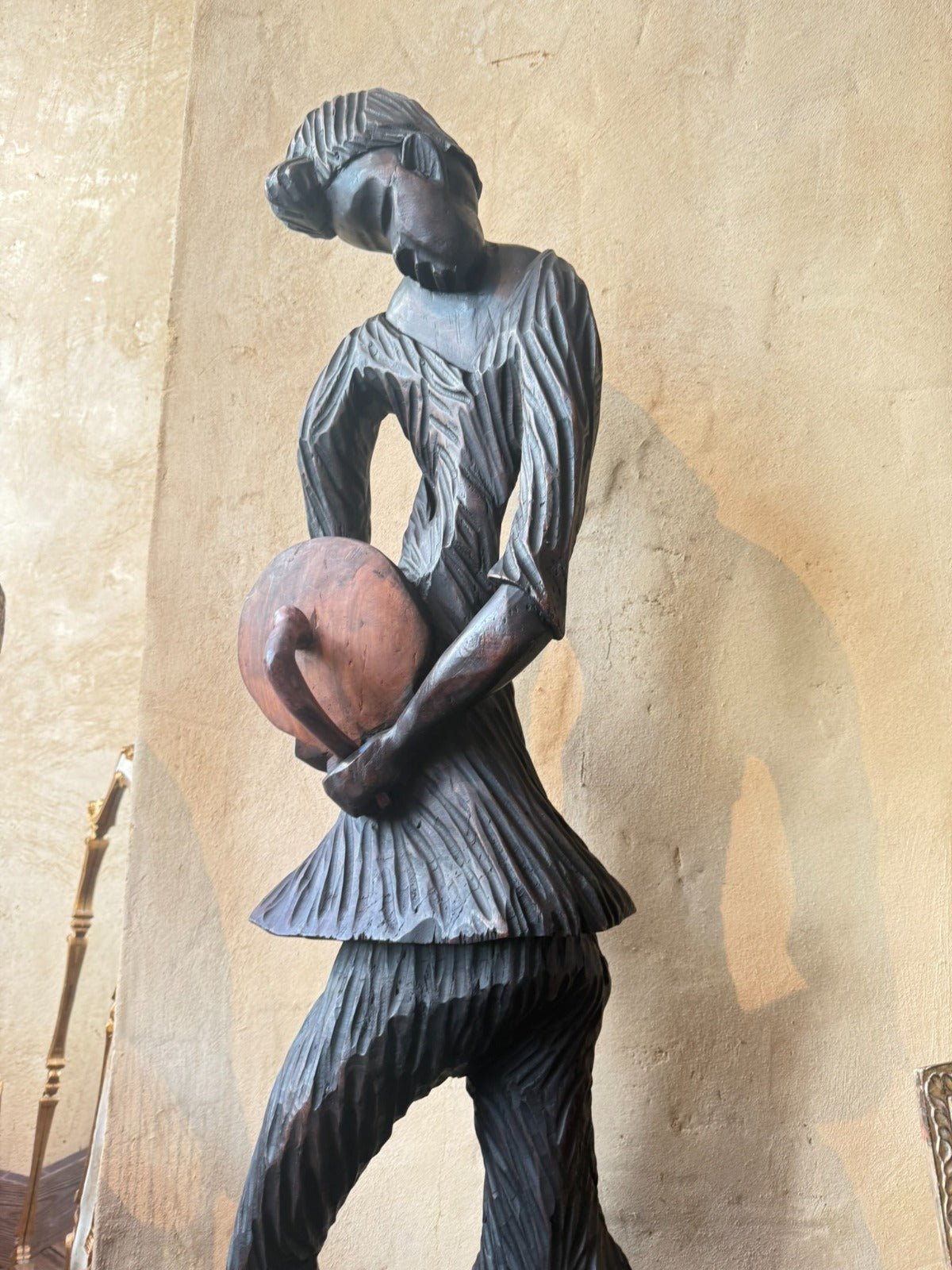 A dark carved wooden figurine of a stylized person holding a reddish-brown sphere, 